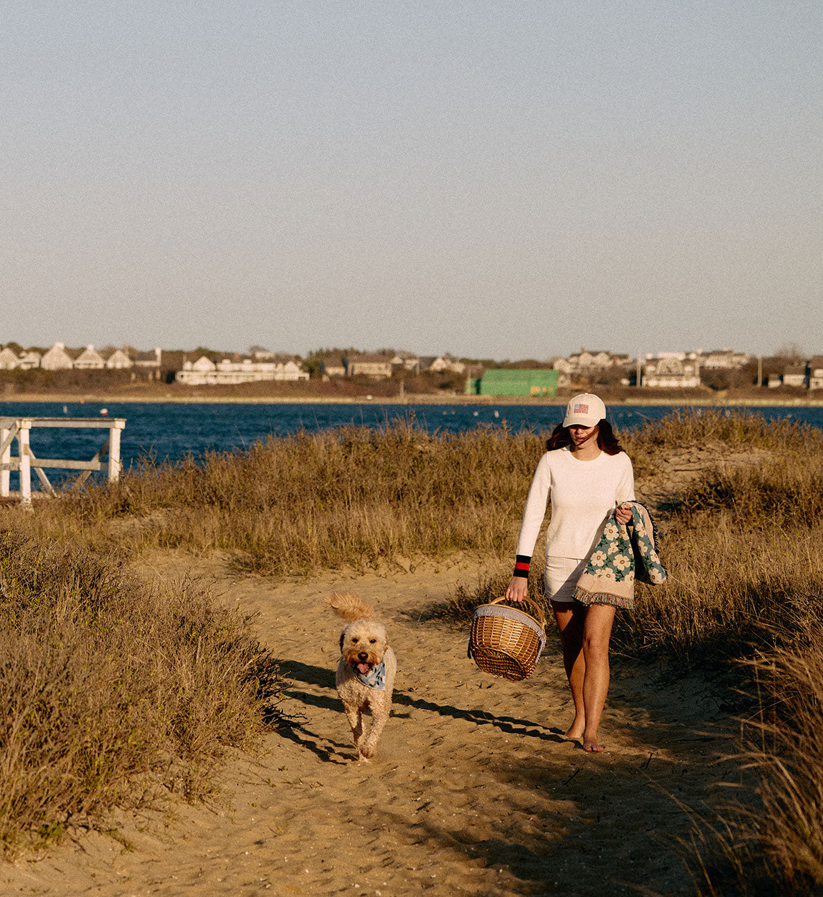 Woman walking a dog on a path by a body of water with houses in the background